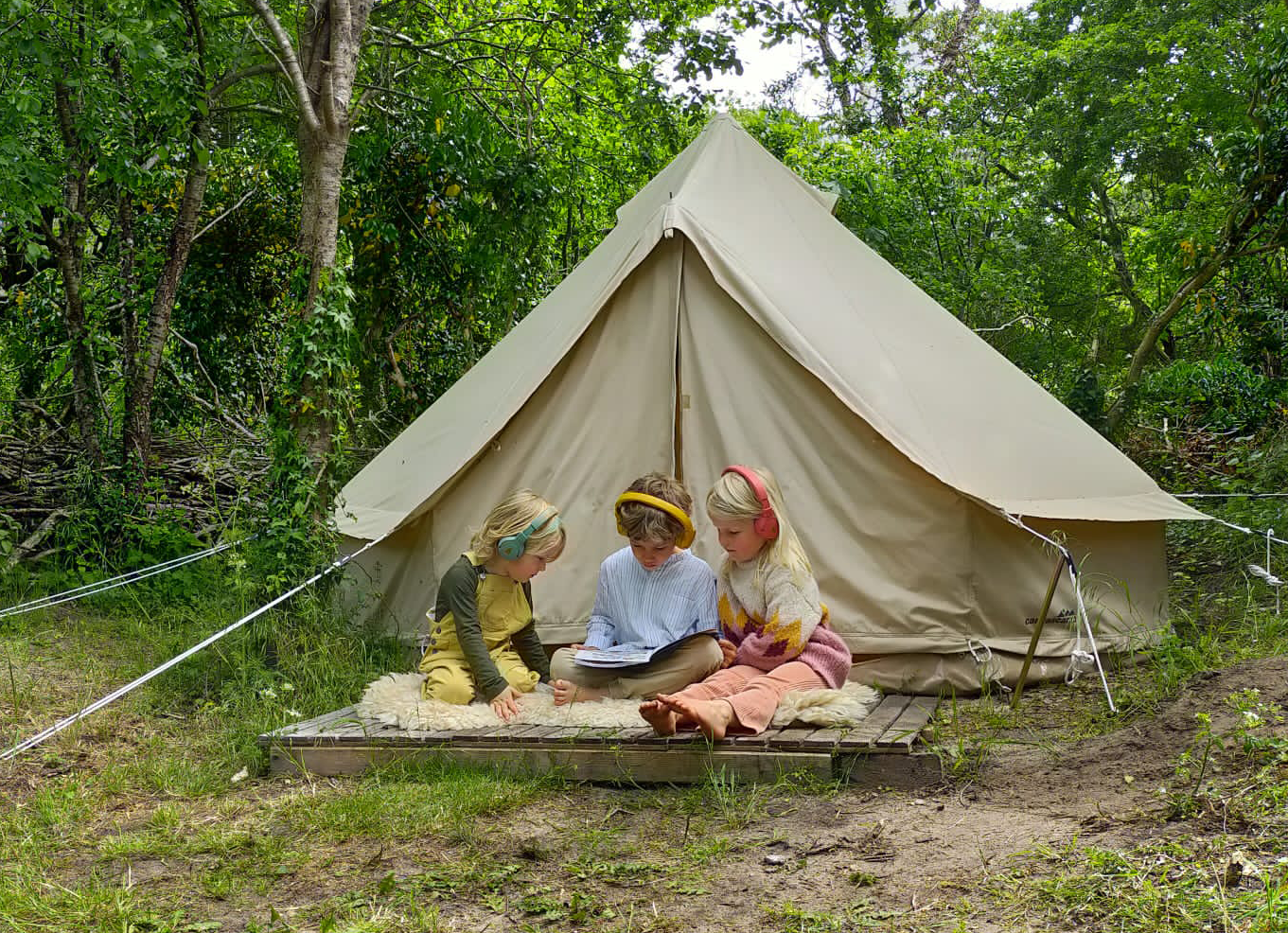 Three kids listening to POGS in front of a tent